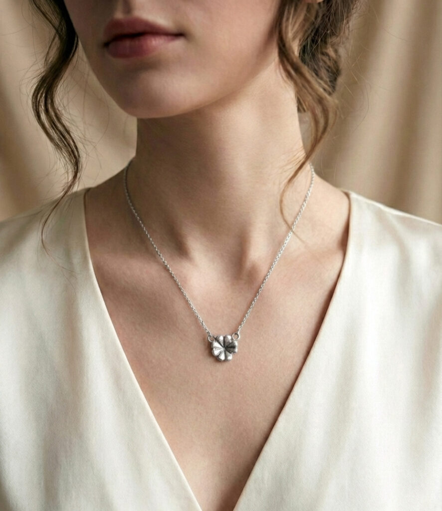 "Colgante mediano de plata de ley 925 con forma de trébol de cuatro hojas, destacando su relieve artesanal y textura orgánica sobre el escote de una modelo."