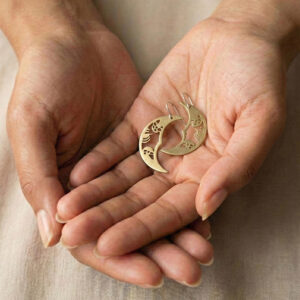 Pendientes de media luna Solsticio de Otoño hechos de latón y plata sostenidos en la mano con luz cálida natural.