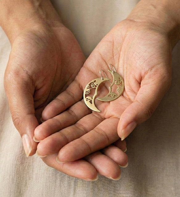 Pendientes de media luna Solsticio de Otoño hechos de latón y plata sostenidos en la mano con luz cálida natural.